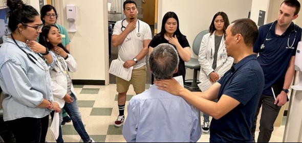 Health professional demonstrating placing hand on neck of a patient to a group of 7 health professionals in a clinical setting.